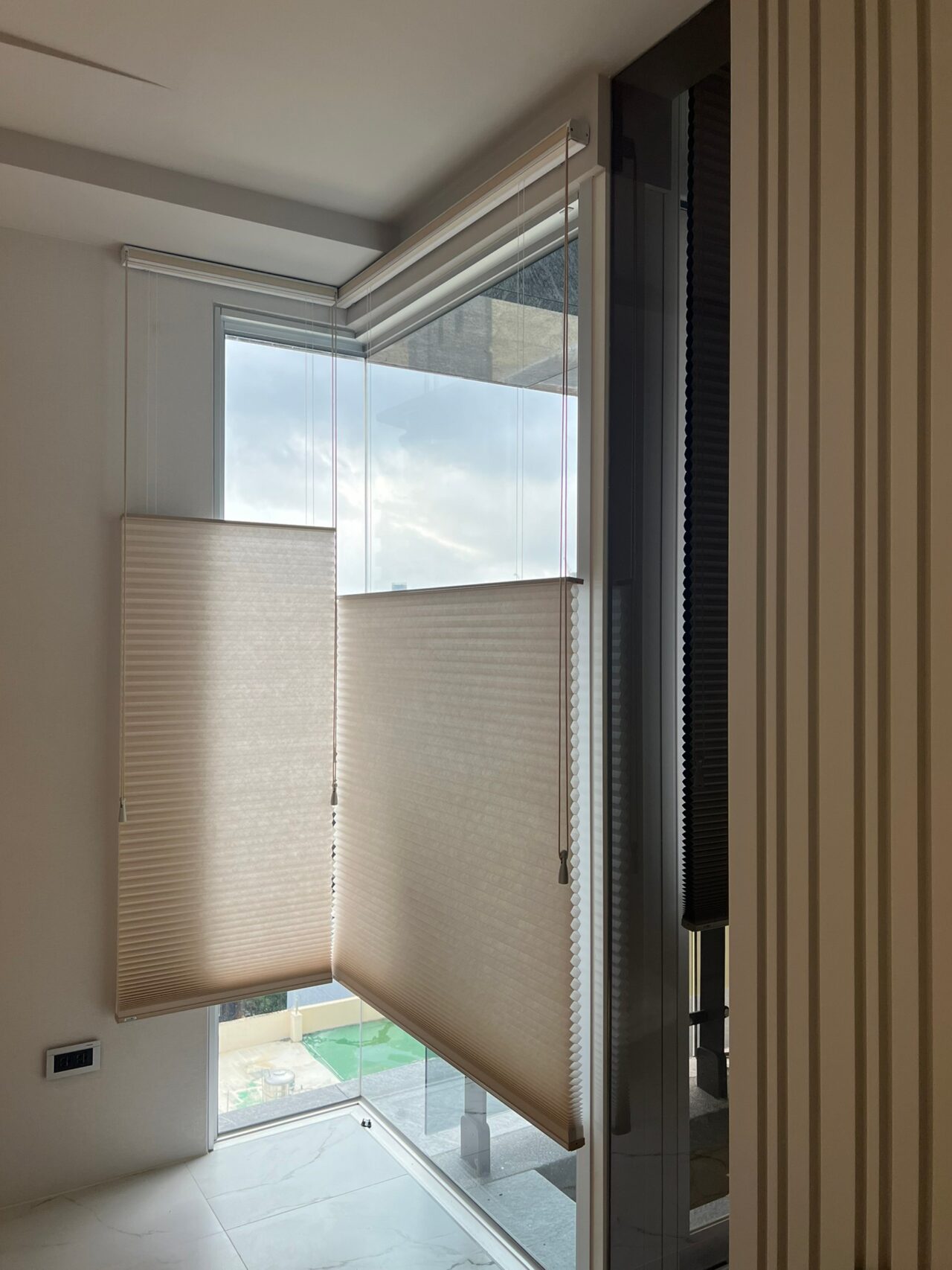 角落 L 型落地窗，讓室內增加自然光線與景觀，因此採用蜂巢簾，可上下移動，隨時調整視線區域內光線，既能保有隱私，也能有採光效果。
